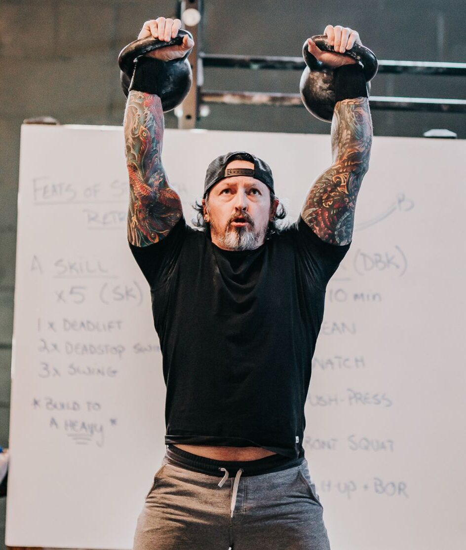 The coach with kettlebells in his hands. There is a whiteboard behind him with information for the exercises.